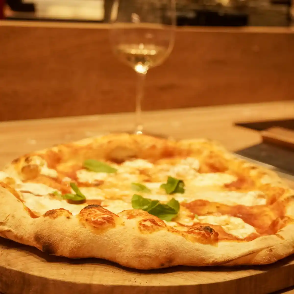 Frische Pizza auf Holz mit einem Glas Weißwein daneben