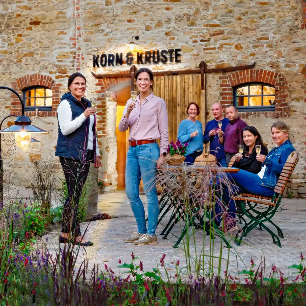 eine Gruppe Menschen steht mit Sektgläsern draußen vor dem Tor von Korn und Kruste