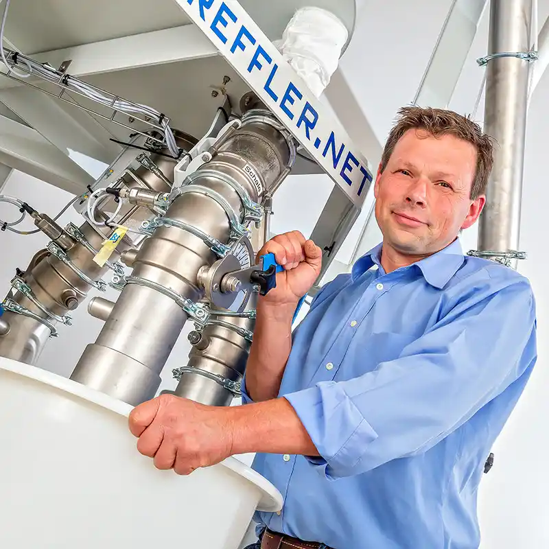 Tillmann steht an der Getreidemühle und hält mit einer Hand den Hebel für die Mühle